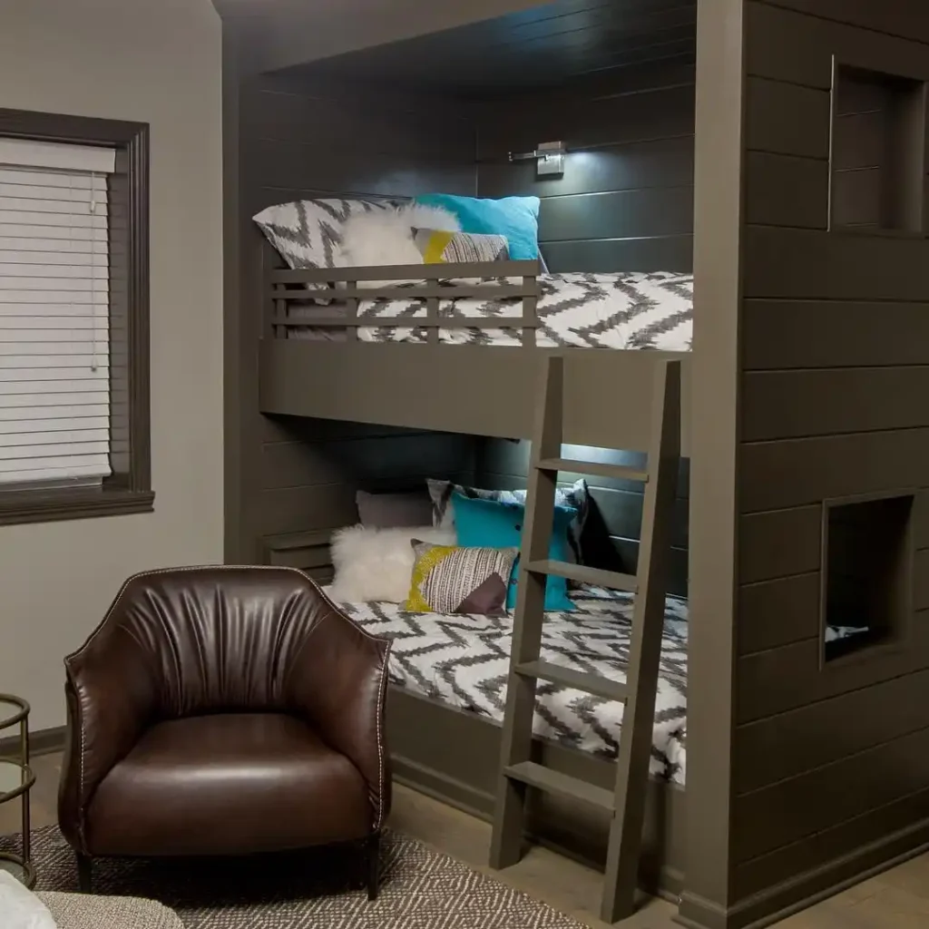 Basement guest bedroom with built-in gray bunk beds and leather armchair.

