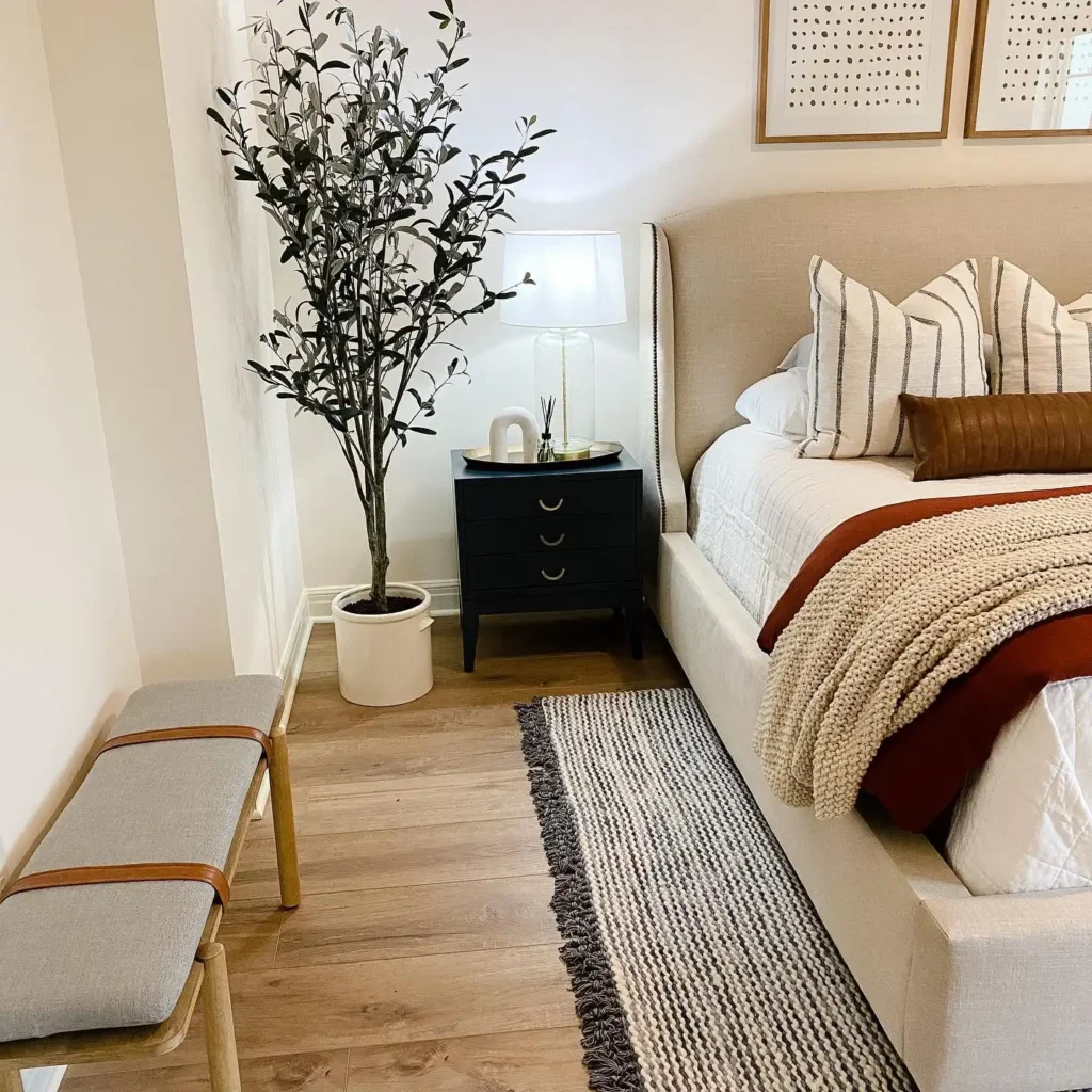 Guest bedroom idea on a budget with warm-toned bedding, striped rug, and potted tree décor.