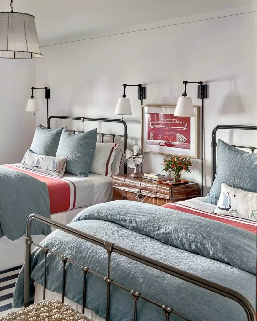 Nautical twin guest bedroom bedding in blue, white, and red accents with iron frames.
