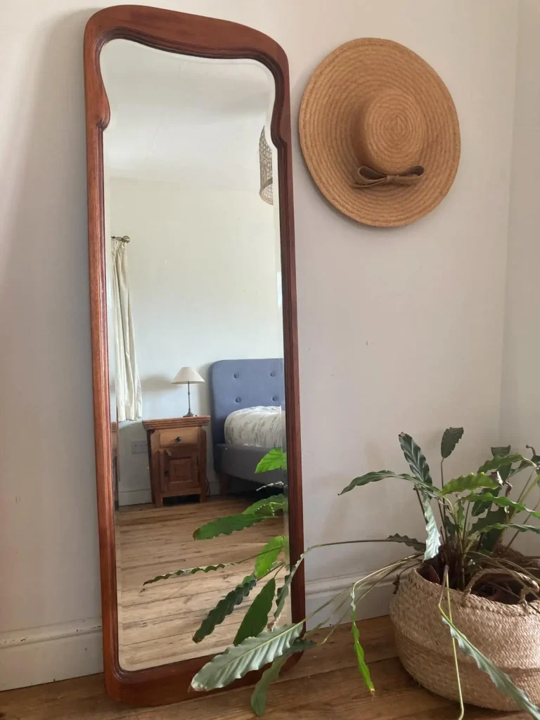 Full length mirror in bedroom with vintage wooden curved frame and greenery