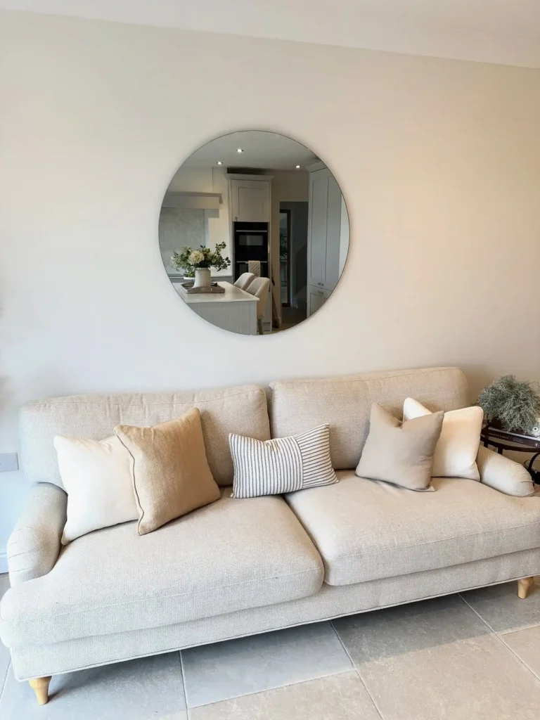 Minimalist living room with round mirror above beige sofa for simple and elegant wall decor ideas above couch.
